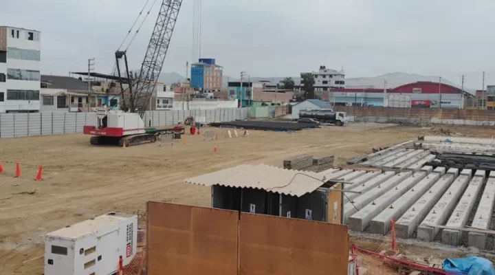 Obra urbana de edificación con la grúa de hincado y el acopio de pilotes prefabricados de concreto ordenados en filas sobre el terreno