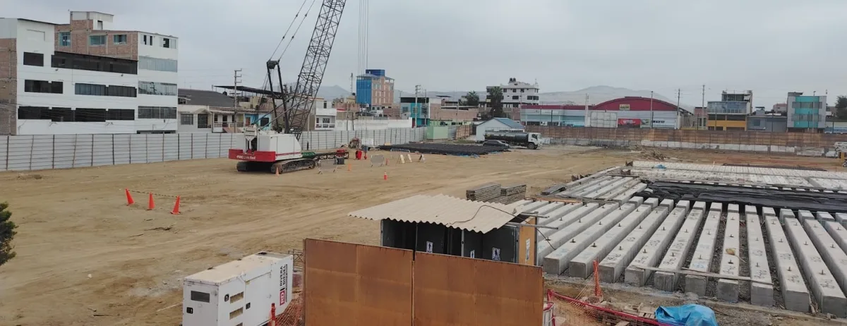Obra urbana de edificación con la grúa de hincado y el acopio de pilotes prefabricados de concreto ordenados en filas sobre el terreno