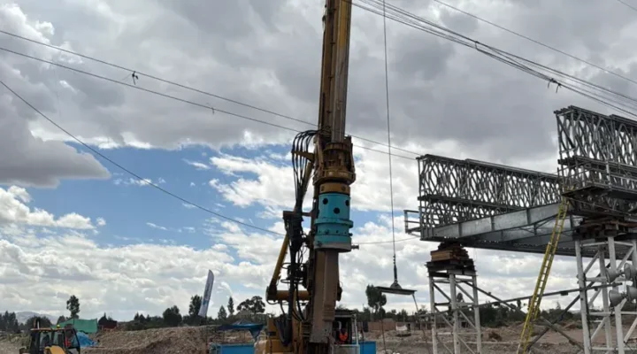 Equipo de perforación ejecutando los pilotes excavados del Puente Cunas, con la estructura del puente al fondo
