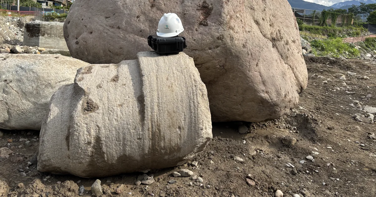 Pilotes excavados en el Puente Victoria: núcleo de roca cortado junto a un bolón de gran tamaño, con un casco como referencia de escala, en San Ramón